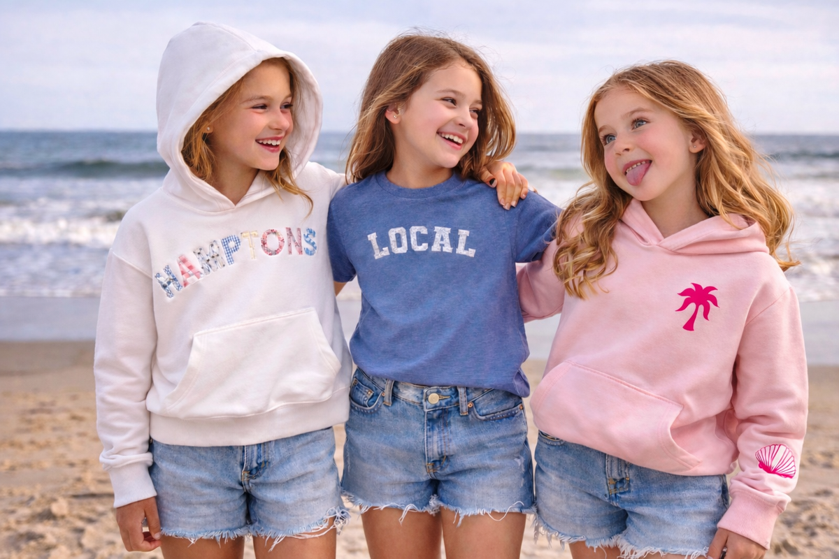 Three children wearing hoodies and shorts on a beach